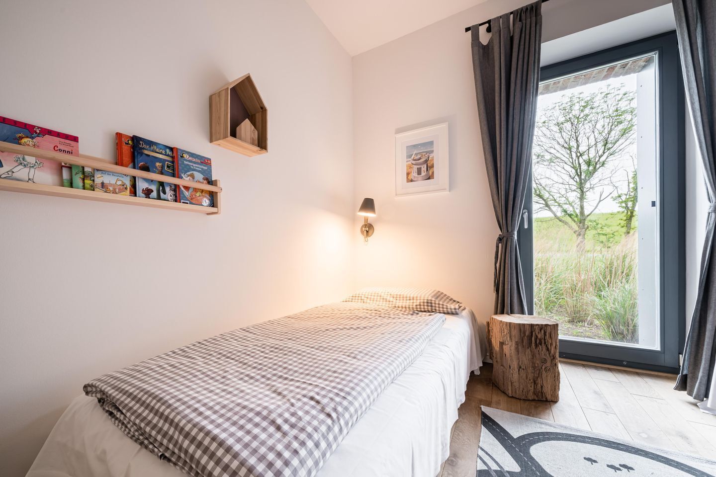 Une chambre à coucher comprenant un lit, une table de chevet, une lampe, une fenêtre avec des rideaux et une bibliothèque remplie de livres.