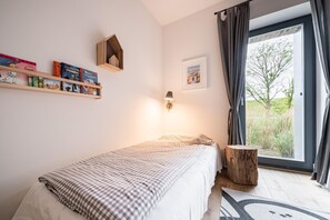 A bedroom with a bed, a bedside table, a lamp, a window with curtains, and a bookshelf with books.