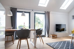 Una sala moderna con comedor, ventanas amplias, un televisor de pantalla plana y suelo de madera.
