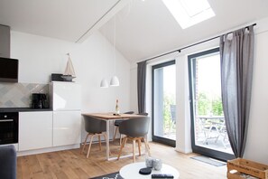 A modern kitchen with white cabinets, a coffee machine, and a dining area with two chairs and a table.