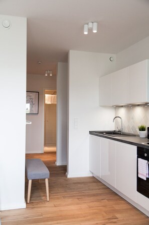 A modern kitchen with white cabinets, a black countertop, and a stainless steel sink. There is a small potted plant on the counter and a towel hanging on the oven door.