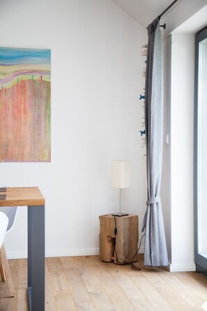 Ein modernes Zimmer mit Holzboden, einem Tisch, einer Lampe und einem Bild an der Wand.