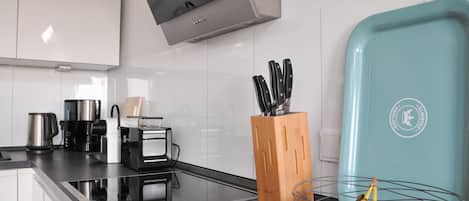 A modern kitchen with white cabinets, a black countertop, a coffee maker, a toaster, and a knife block.