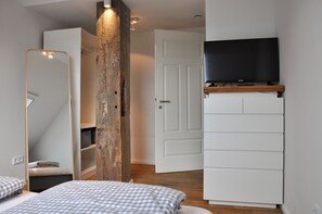 Une chambre avec un grand miroir, un pilier en bois, une armoire blanche et un téléviseur posé sur une étagère en bois.