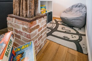 Una sala acogedora con una chimenea de ladrillo, un sillón de peluche gris y una alfombra con motivos de carretera.