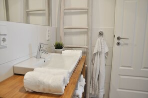 Ein modernes Badezimmer mit einem großen weißen Waschbecken, einer Holzkommode, einer Topfpflanze und einem Handtuchhalter.