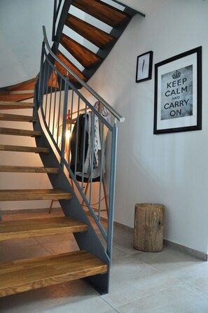 A spiral staircase with wooden steps and a metal railing, a framed motivational quote on the wall, and a wooden stump beside the stairs.