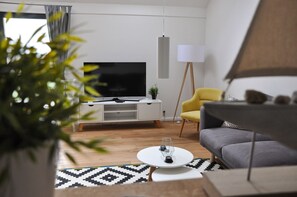 Una sala de estar moderna con un televisor de pantalla plana, un sillón amarillo, un sofá gris y una lámpara de pie.