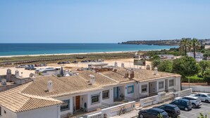 Uma área residencial costeira com edifícios de telhado em terracota, uma praia e um céu claro.