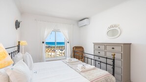 Quarto com cama, penteadeira, espelho e vista para a praia.