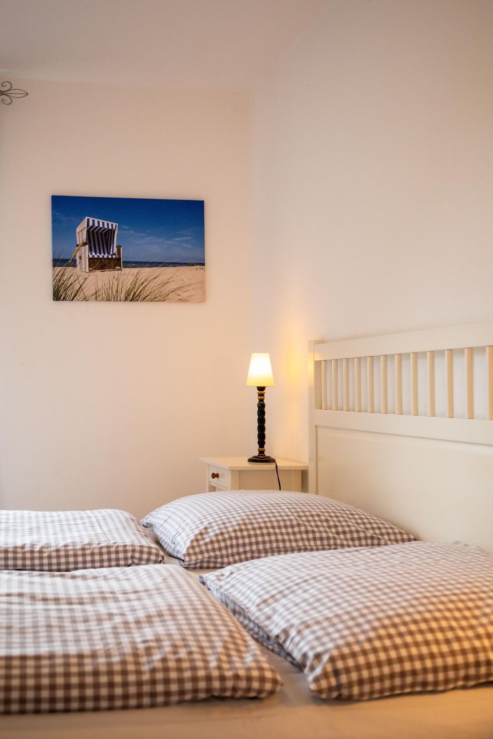 Un dormitorio con dos camas, una mesita de noche con lámpara y un cuadro de una playa en la pared.