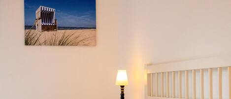 Un dormitorio con dos camas, una mesita de noche con lámpara y un cuadro de una playa en la pared.