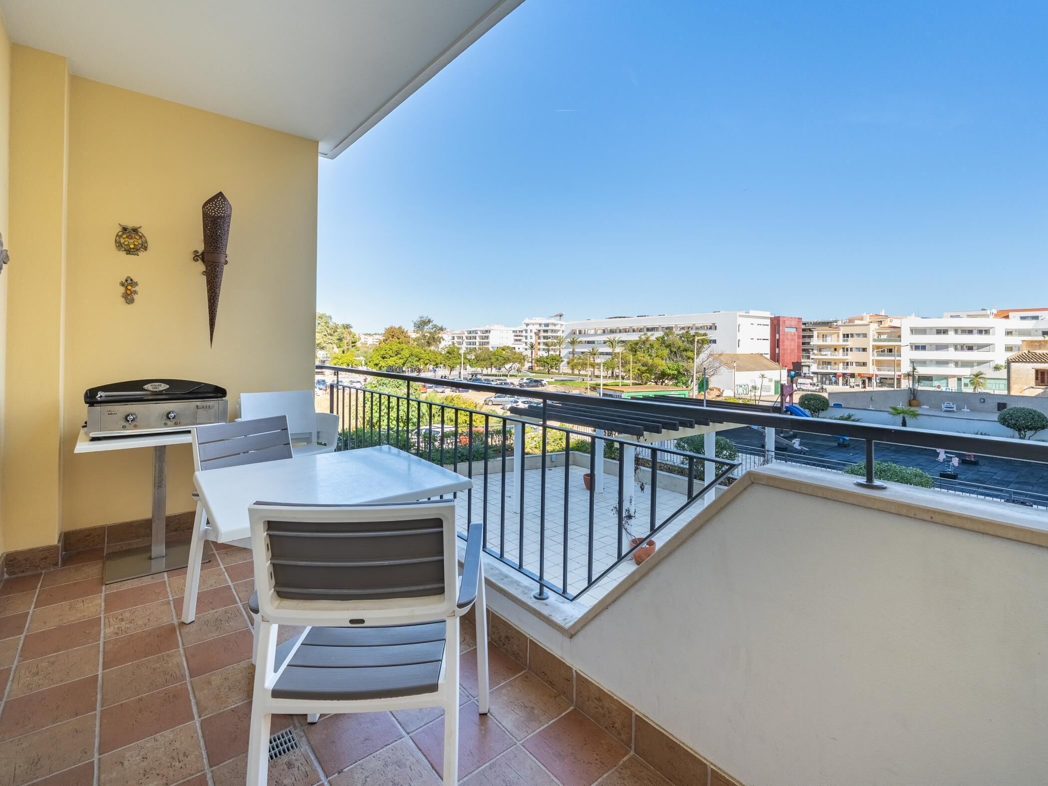 Een balkon met een tafel, stoelen, een barbecue en decoratieve wandkunst.