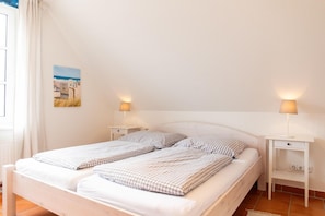 A double bed with checkered bedding, two bedside tables with lamps, a small nightstand, and a wall-mounted picture.