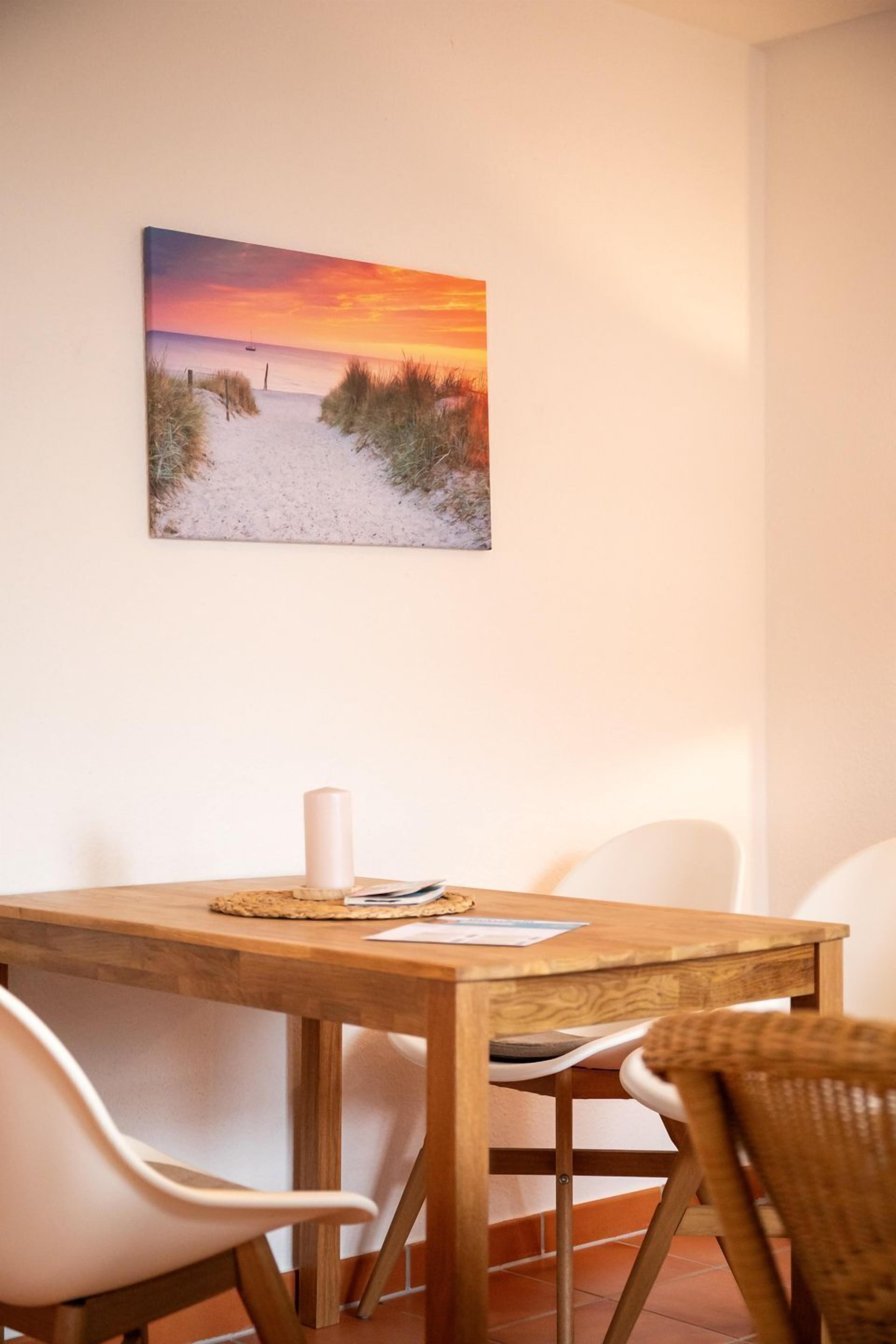 A dining area with a wooden table, white chairs, and a painting of a beach scene.