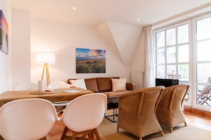 A modern living room with a dining area, a sofa, and a large window with a view.