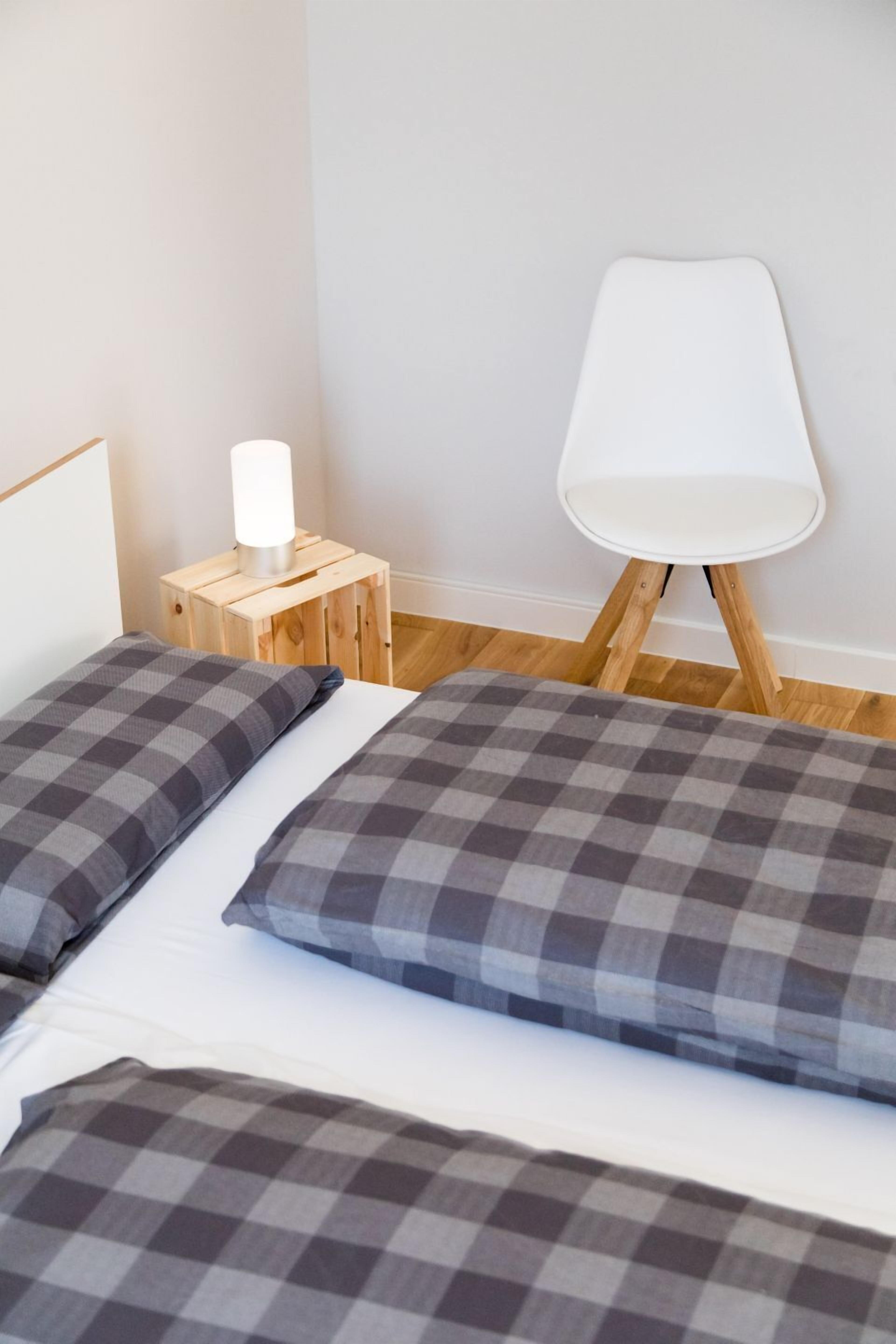 Een slaapkamer met twee bedden, een nachtkastje met een lamp en een witte stoel.