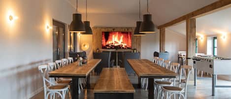 Un comedor amplio con una larga mesa de madera, sillas blancas, iluminación colgante y una chimenea.