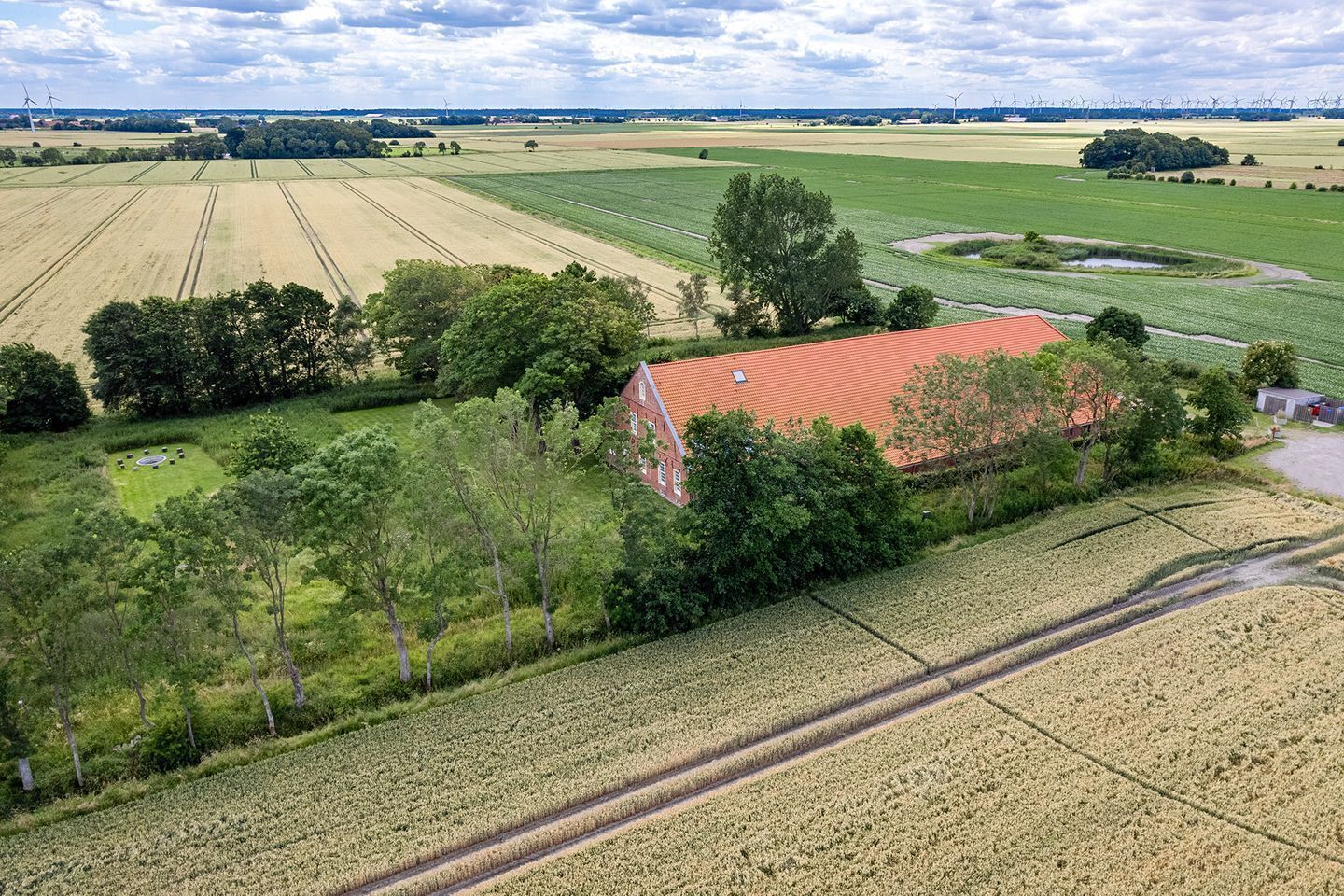 Paesaggio rurale con campi, alberi e un edificio con tetto rosso.