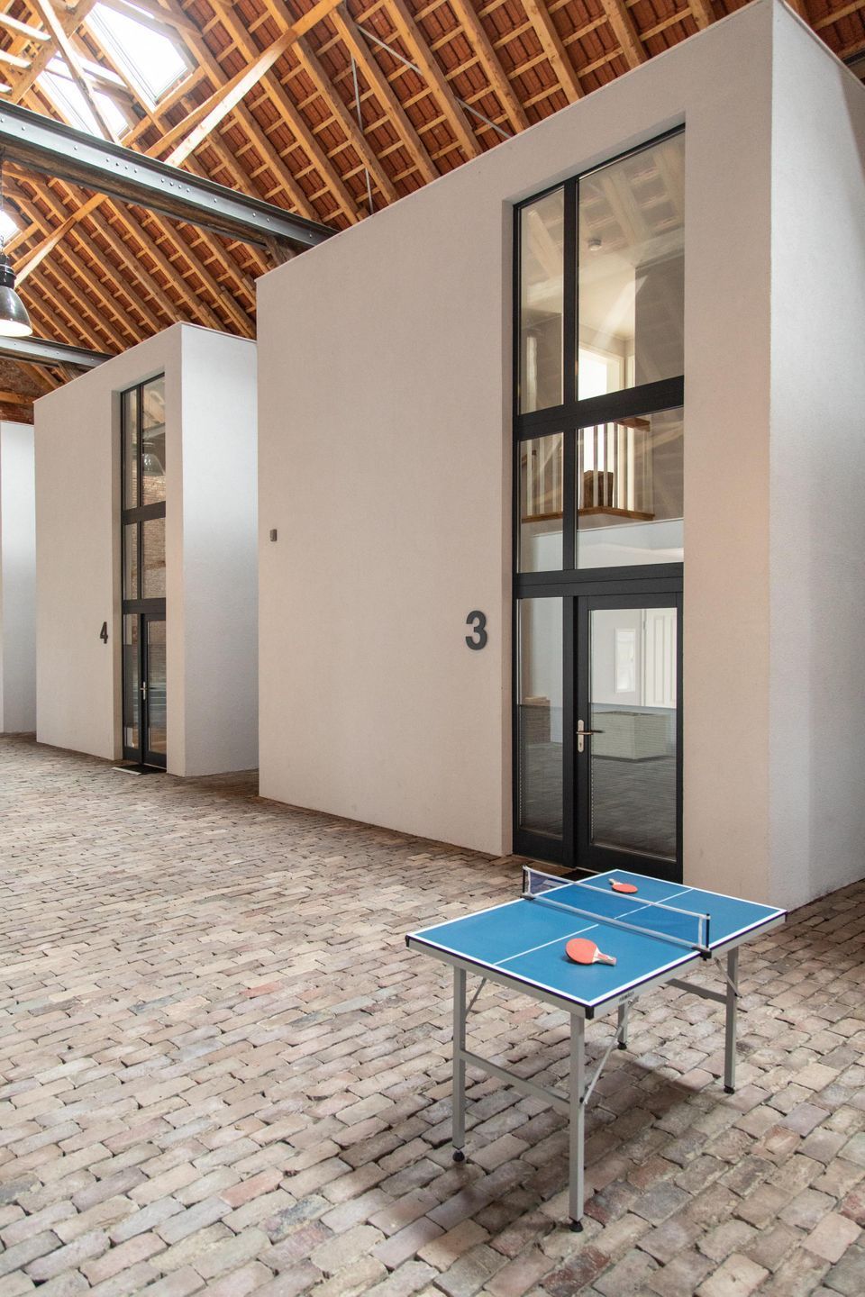 Een gang met genummerde deuren, een pingpongtafel en een hoog houten plafond.