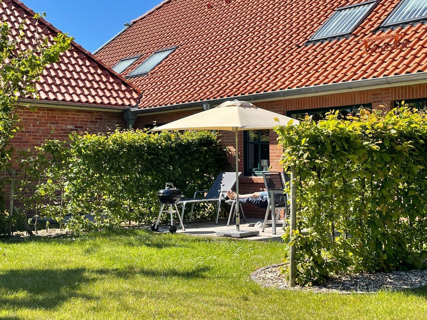 A brick house with a tiled roof, a patio with a table and chairs, and a lawn.