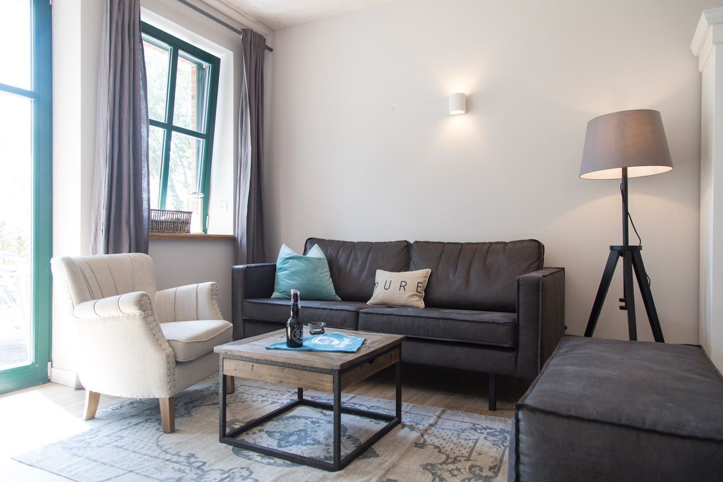 Uma sala de estar com sofá, poltrona, mesa de centro, abajur e uma janela com cortinas.