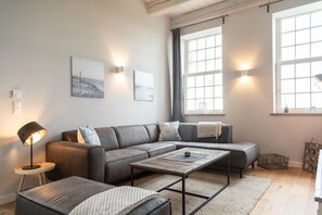 Een moderne woonkamer met een grijze bank, een salontafel en een vloerlamp.
