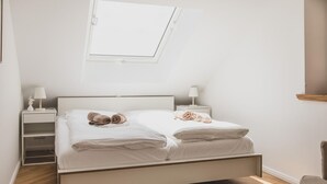 A bedroom with a bed, two bedside tables, a nightstand, a window, and a chair. - Traumhafte Fewo mit Terrasse im Historischen Hof - Gulfhof Boomgaarden (Krummhörn)