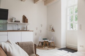 A modern kitchen with white cabinets, a wooden countertop, and a built-in TV. There is a dining area with two white chairs and a small table. - Traumhafte Fewo mit Terrasse im Historischen Hof - Gulfhof Boomgaarden (Krummhörn)