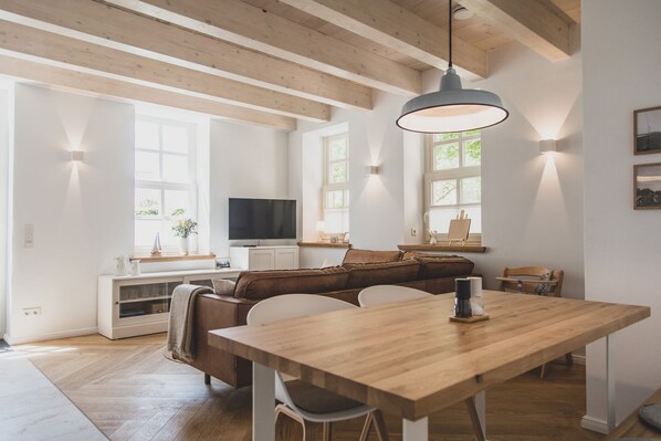 A modern living room with a wooden dining table, a brown leather sofa, and a television.