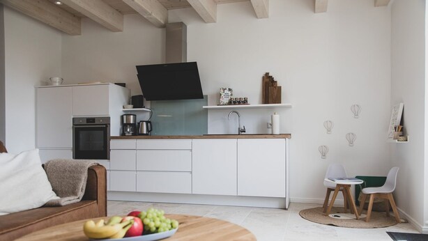 A modern kitchen with white cabinets, a black range hood, and a wooden countertop.