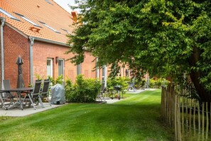 A brick building with a red-tiled roof, a grassy yard, and outdoor furniture including a table and chairs.