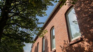 A red brick building with large windows and a tree in the foreground.