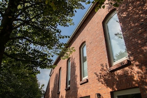 A red brick building with large windows and a tree in the foreground.
