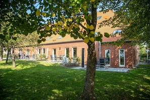 A brick building with a tiled roof, outdoor seating, and a well-maintained lawn.