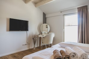 Una habitación de hotel con cama, escritorio, silla, televisión y ventana con cortinas.