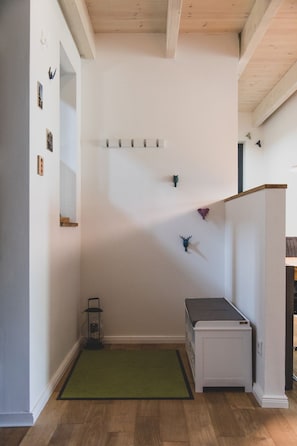 Una habitación con piso de madera, un tapete verde, un armario blanco y una estantería con objetos decorativos.