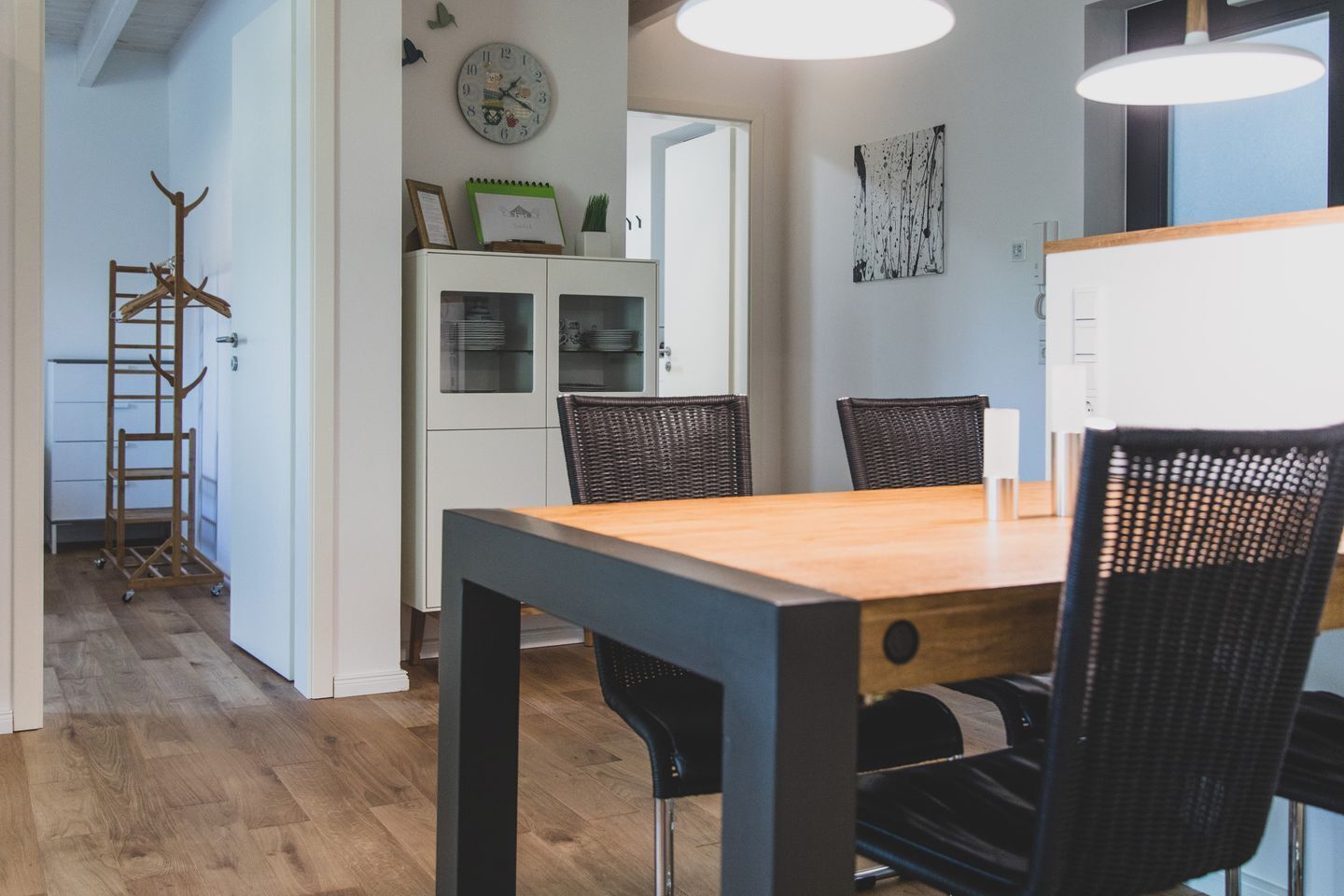 A dining area with a wooden table and black chairs, a white cabinet with glass doors, and a wall clock.