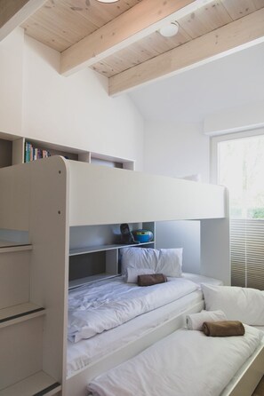 Ein Etagenbett mit Schreibtisch und Regalen, ein Fenster mit Jalousien und eine Decke mit Holzbalken.