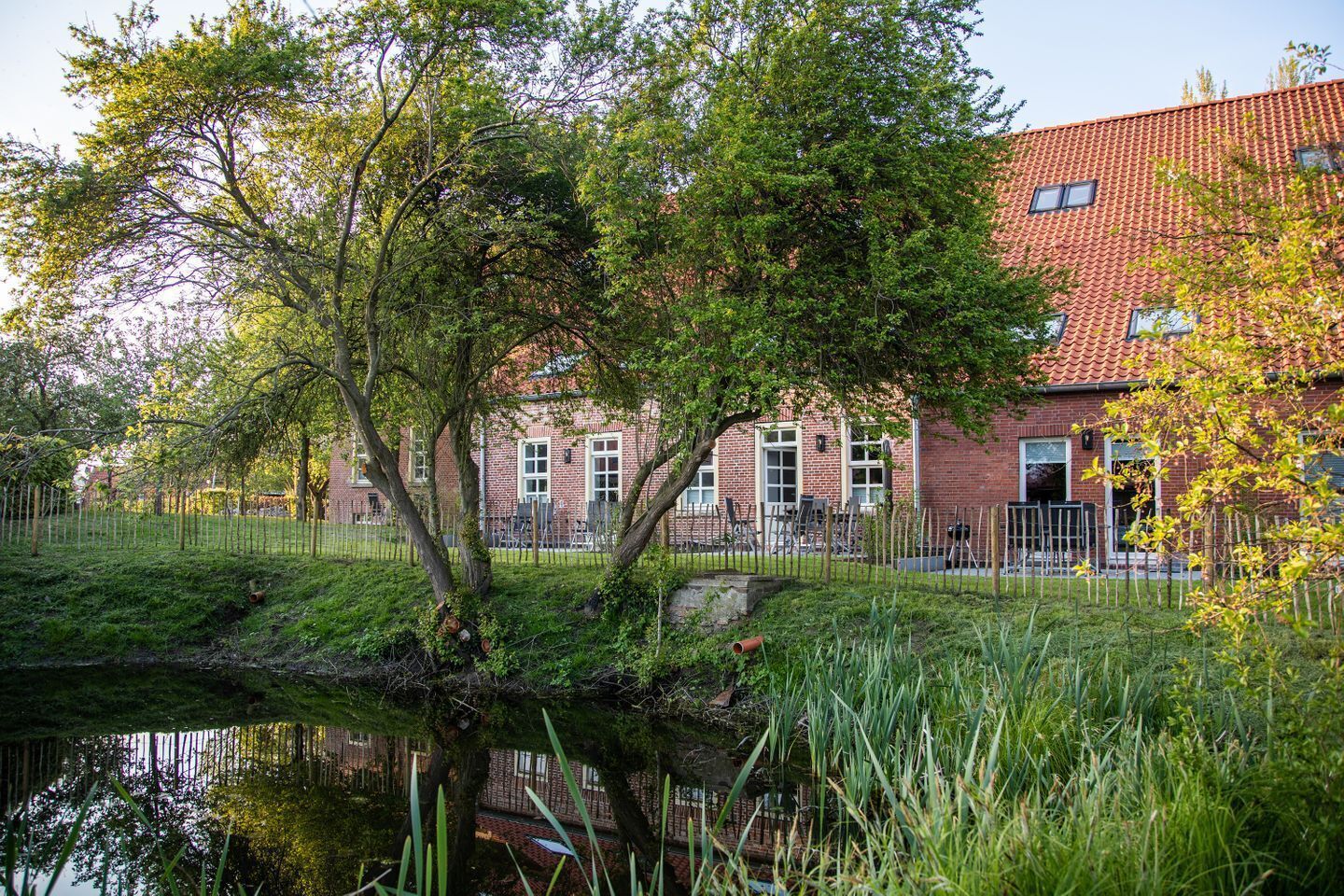 A brick building with a red-tiled roof, surrounded by trees and a small pond.
