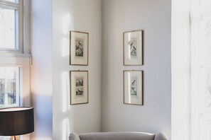 Ein Zimmer mit Fenster, einer Lampe und vier gerahmten Vogelbildern an der Wand.