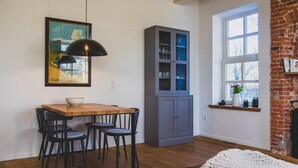 Ein Essbereich mit Holztisch und schwarzen Stühlen, eine graue Schranke mit Glastüren sowie ein großes Fenster mit Blick auf Bäume.