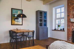 Ein Essbereich mit Holztisch und schwarzen Stühlen, eine graue Schranke mit Glastüren sowie ein großes Fenster mit Blick auf Bäume.