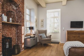 A cozy room with a brick wall, a wooden dresser, a grey sofa, a TV, and a window with framed pictures.