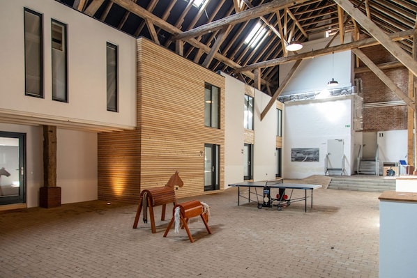 A spacious interior with exposed wooden beams, a ping pong table, and a horse sculpture.