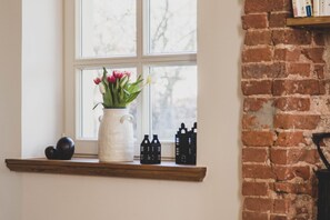 Ein Fenster mit einer weißen Vase mit Blumen, ein Holzregal mit schwarzen Dekoartikeln und eine Ziegelwand.