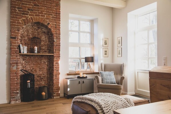 A cozy room with a brick fireplace, a comfortable armchair, a wooden table, and a bookshelf.