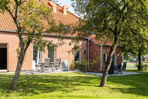 A brick building with a tiled roof, outdoor seating, and trees.
