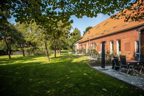 A brick building with a tiled roof, a grassy lawn, and a patio with outdoor furniture.