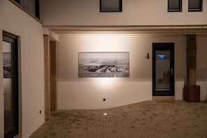 A hallway with a black and white photograph on the wall, a door with a glass panel, and a brick floor.
